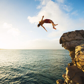 person doing a backflip off a cliff into the water